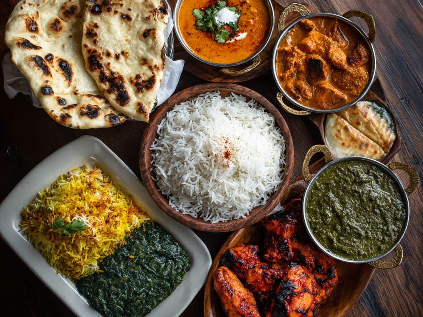 Een gedekte tafel met naan, basmatirijst, biryani, saag en drie curry&rsquo;s in koperen schaaltjes.