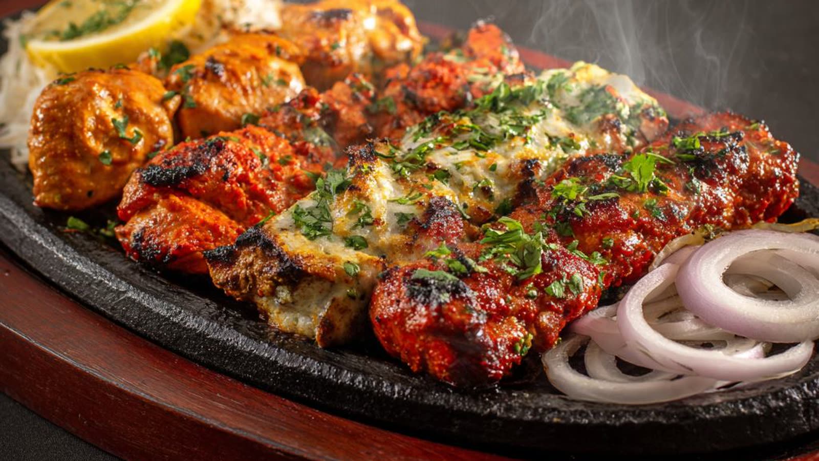 Een sissende plaat met tandoori kip, lamb tikka en seekh kebab uit de kleioven.